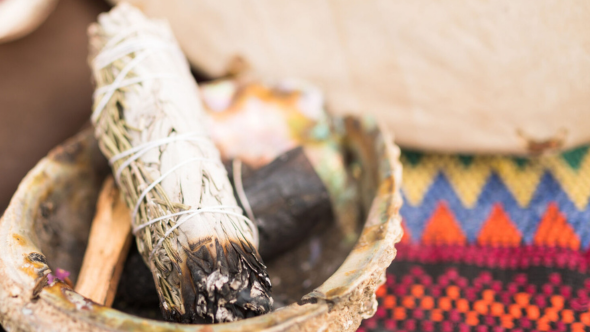 A white sage smudge stick is placed on a conch with Indigenous textiles in the background