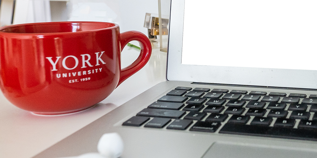 Red York University latte mug beside a laptop