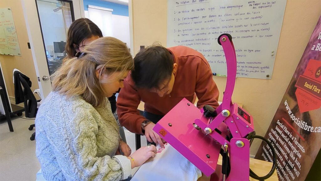 Un groupe diversifié d'individus collaborant sur une presse à chaud rose vif pour fabriquer un T-shirt.