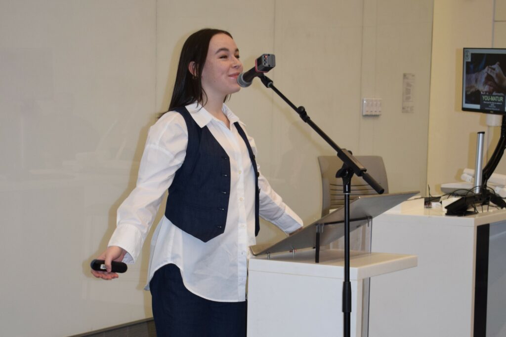 Un étudiant s'exprimant en toute confiance sur un podium avec un microphone, s'adressant à un public.