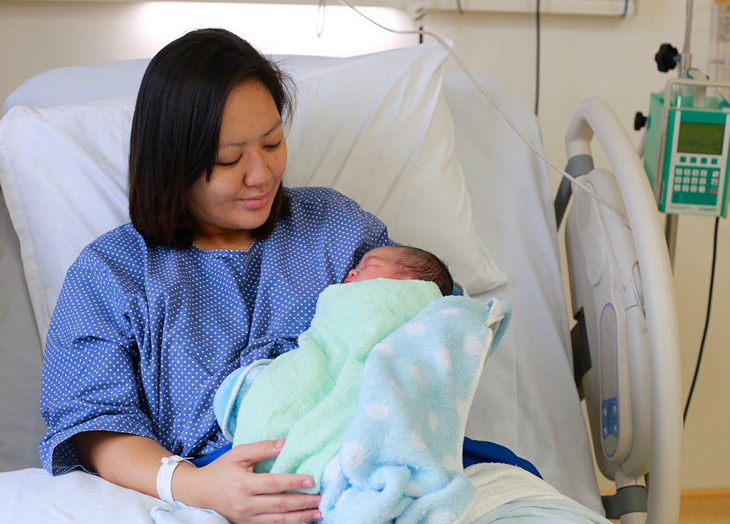 Mother holding baby in a hospital bed.