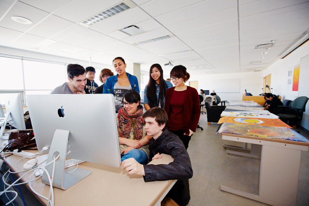 A group of students sitting around a computer monitor. 