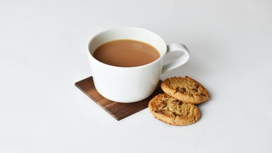 A cup of chai latte and cookies on a wooden coaster