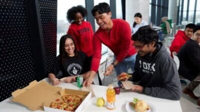 Four students wearing York university merchandise sharing a pizza