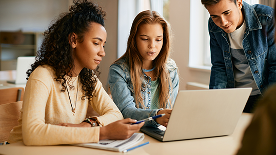 Group of students cooperating while e-learning on laptop in the classroom