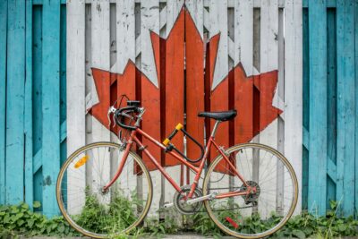 Bicycle leaning against Canadian Flag. The photo is by Ali Tawfiq on Unsplash.