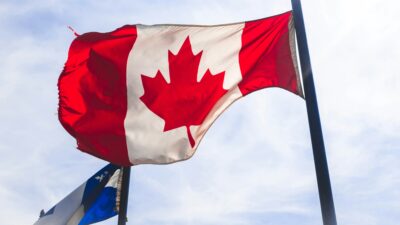 Canadian and Quebec flag in the wind. The photo is by Ryan on Unsplash.