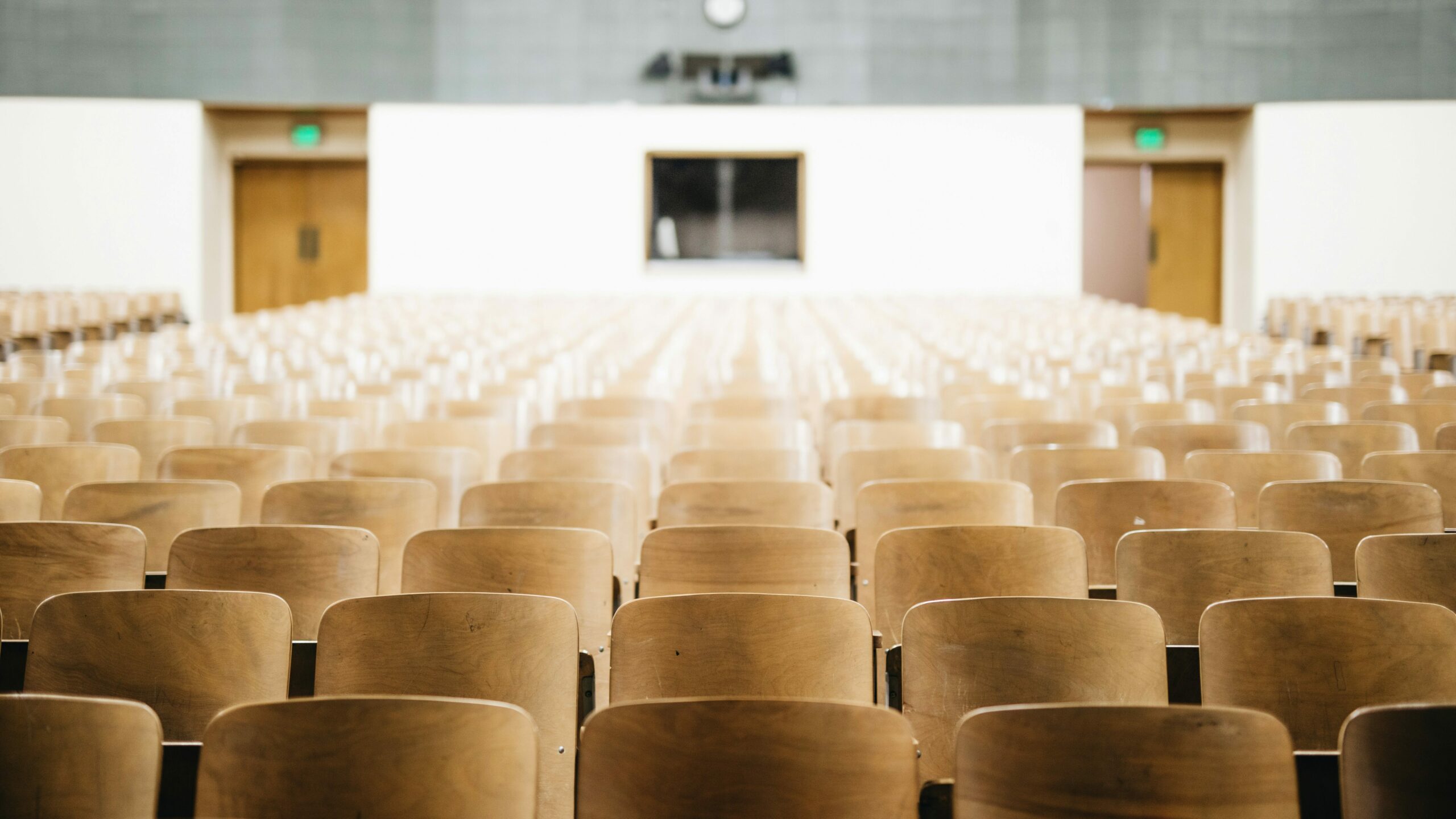 Photo of lecture hall with wooden chairs. Photo: Nathan Dumlao on Unsplash.