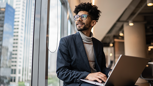 A man on a laptop staring out a window and smiling