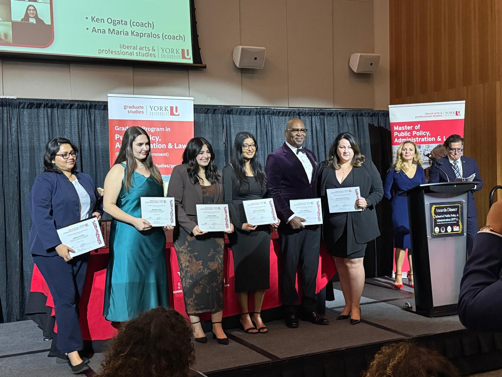 Students receiving recognition awards from the professors on stage.