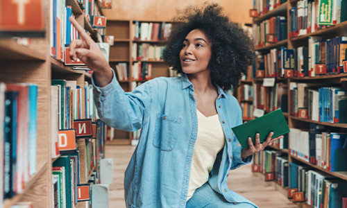 black girl sitting on floor of library looking at shelves