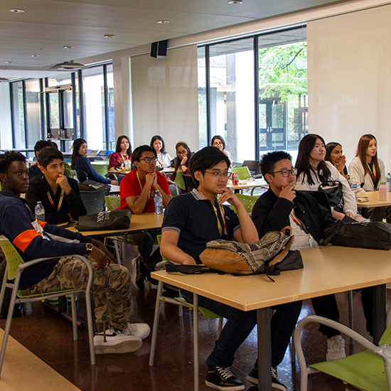 Students sitting at desks listening to a presentation by Associate Dean MJ Maciel Jorge.