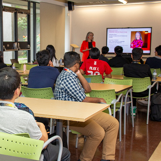 Students sitting at desks listening to a presentation by Associate Dean MJ Maciel Jorge.