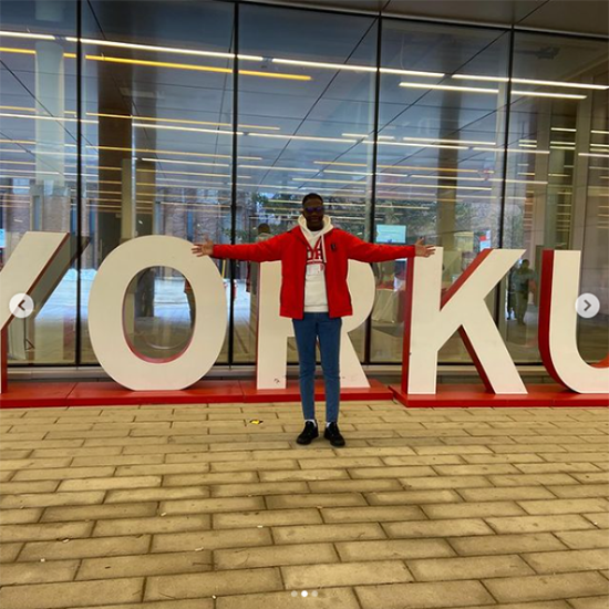 Student standing in front of the York U sign with their arms stretched out.