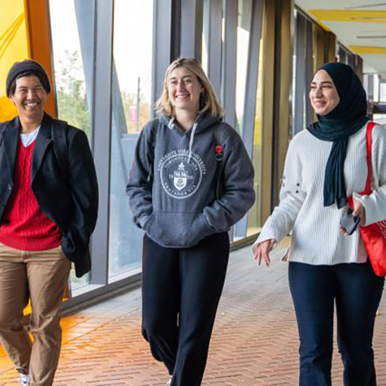 Three students walking down a York U hallway, talking to each other.