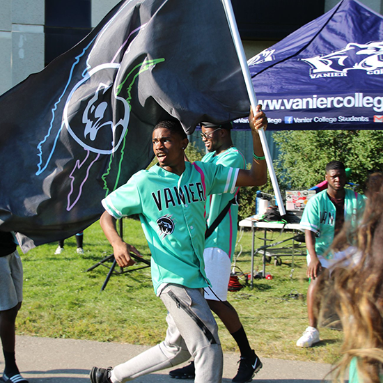 Vanier College student running outside with the Vanier College flag.