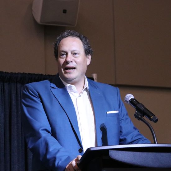 Dean J.J. McMurtry standing on stage behind a podium speaking into a mic.