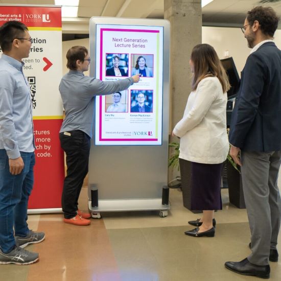 Four people standing in front of a digital kiosk looking at their pictures on it.