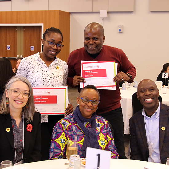 Two students posing with their certificate of completion from the Advancing YU program, standing with Faculty and Staff members.