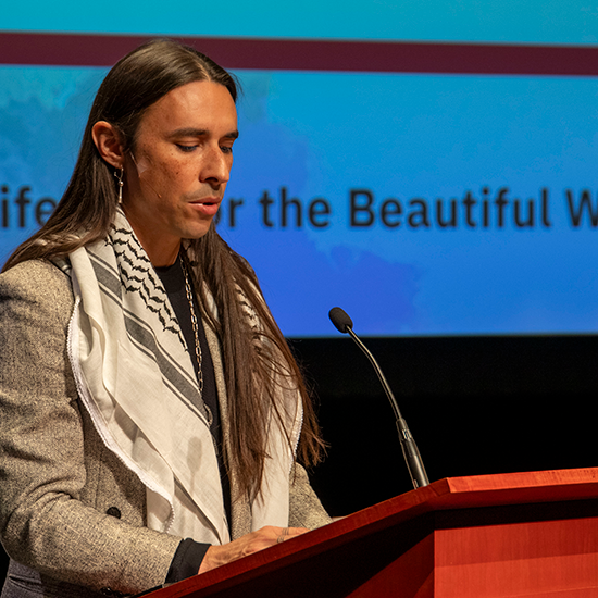 Speaker standing on stage behind a podium, speaking into a mic.