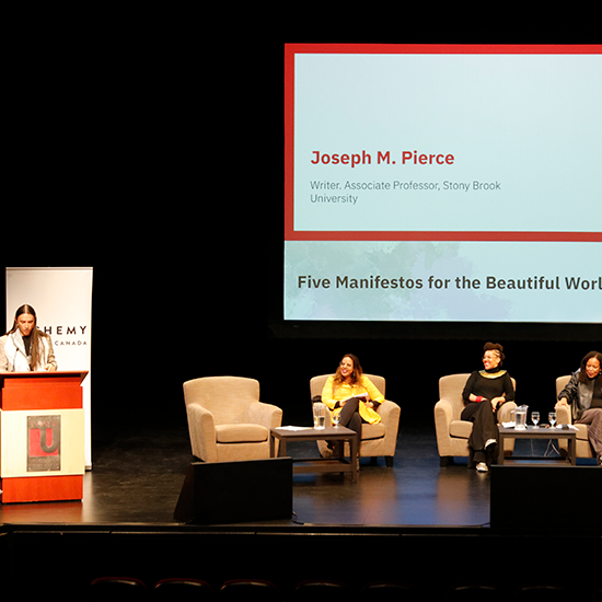 Panelists sitting on stage, looking at speaker standing behind a podium and delivering their lecture.