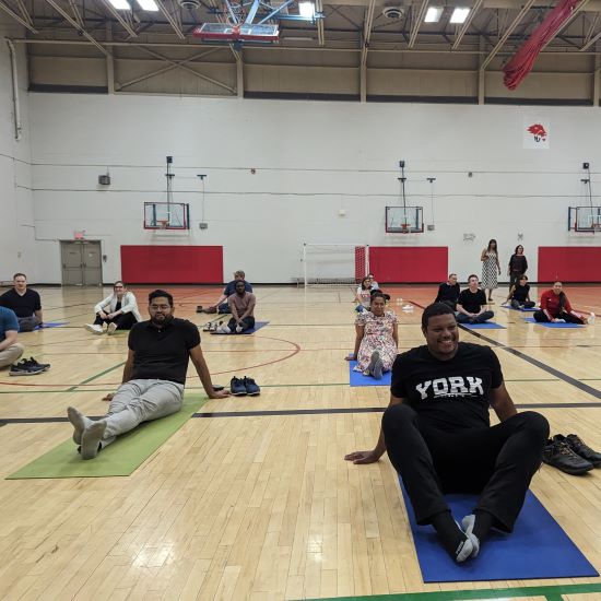 Managers sitting on yoga mats on the floor of a school gym.