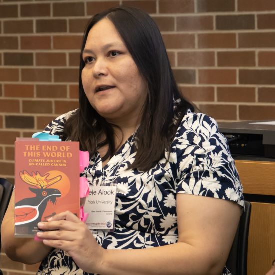 Person sitting down, hold up a book, speaking to a group.