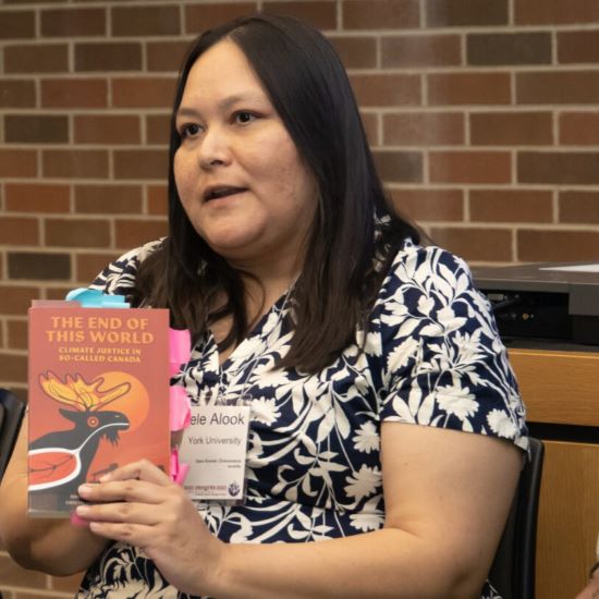 Person sitting down, hold up a book, speaking to a group.