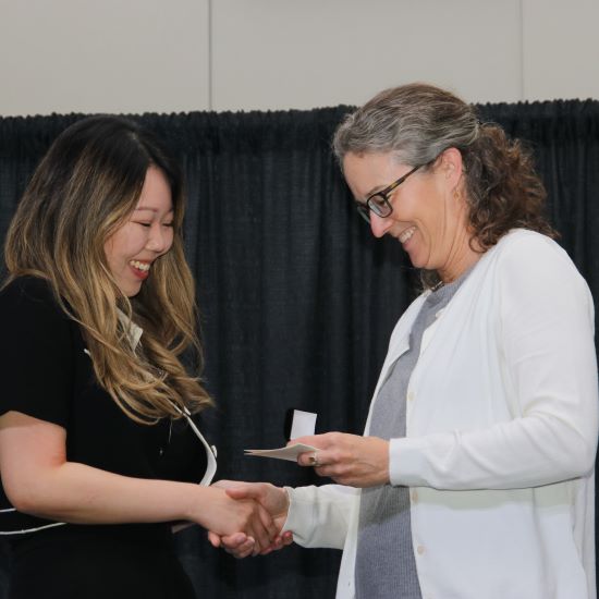 Staff member shaking hands with Associate Dean Maggie Quirt, as she hands her a pin.