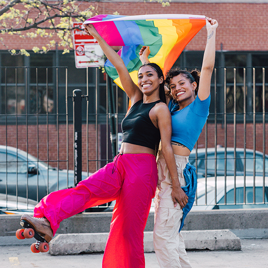 Two women on roller skates with a rainbow flag