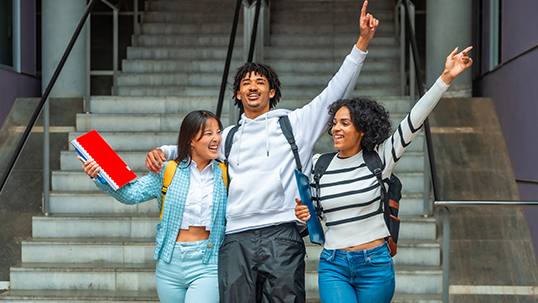 Three multi-ethnic students celebrating raising hands together outdoors the university