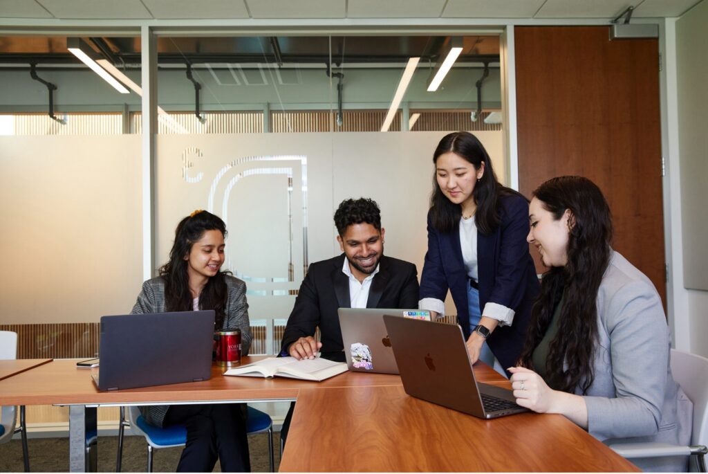 Four students with laptops looking at one screen 