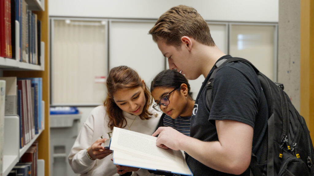 A young male and two female students looking at a open book