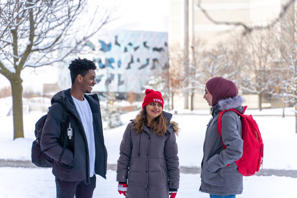 Three students speaking outside on sunny, but snowy day.