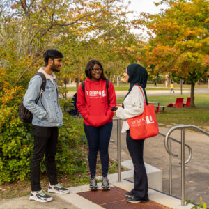 Three students speaking happily with each other next to a garden.