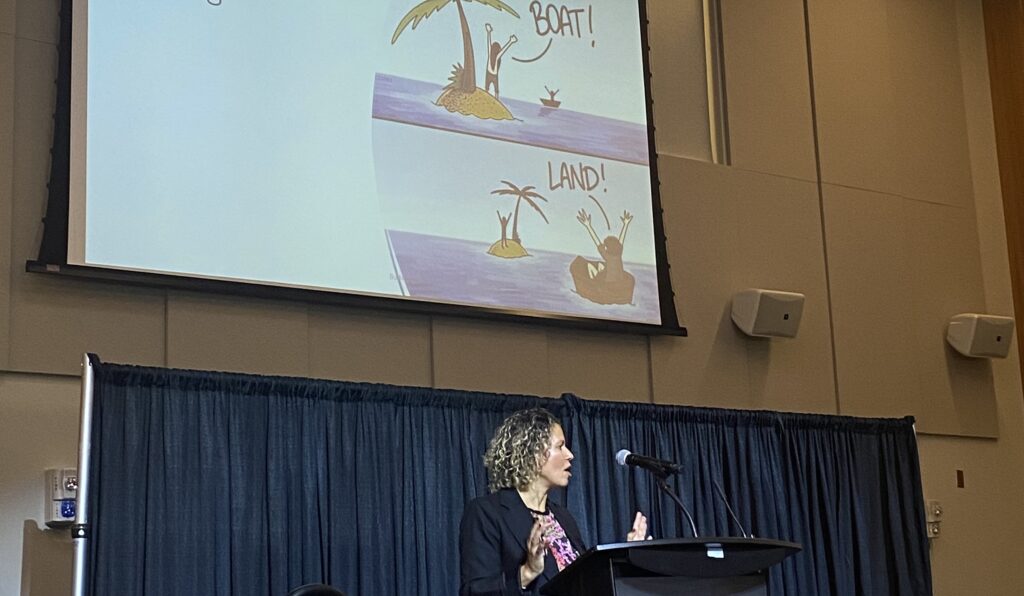 speaker giving presentation on stage with screen behind her 