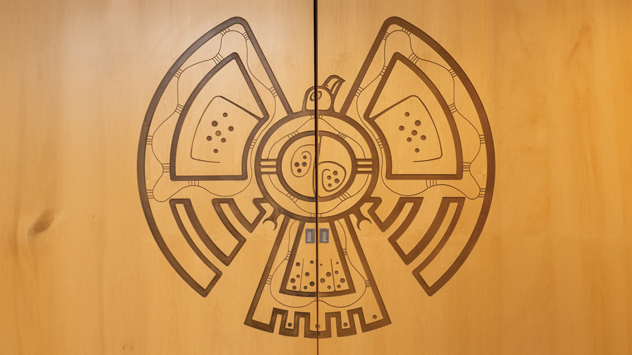 Image of light two panel door with Indigenous artwork of a carved eagle in the middle