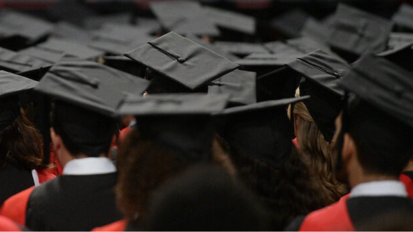 A  group of grad caps as graduating students face away from the camera in a crowd