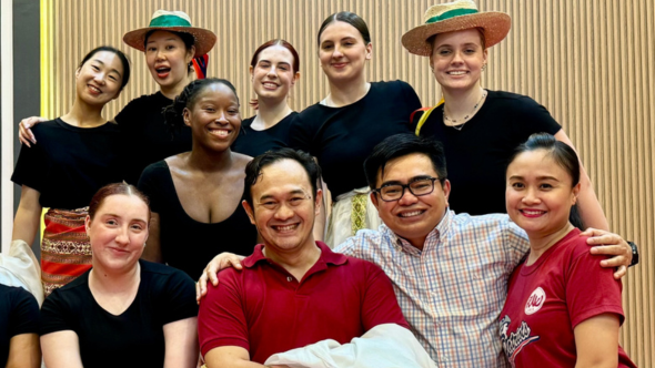 A diverse group of students wearing black tops, some with hats and three professors in a group