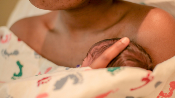 A newbord baby cuddles up to its mother's bare chest with a blanket wrapped around them.