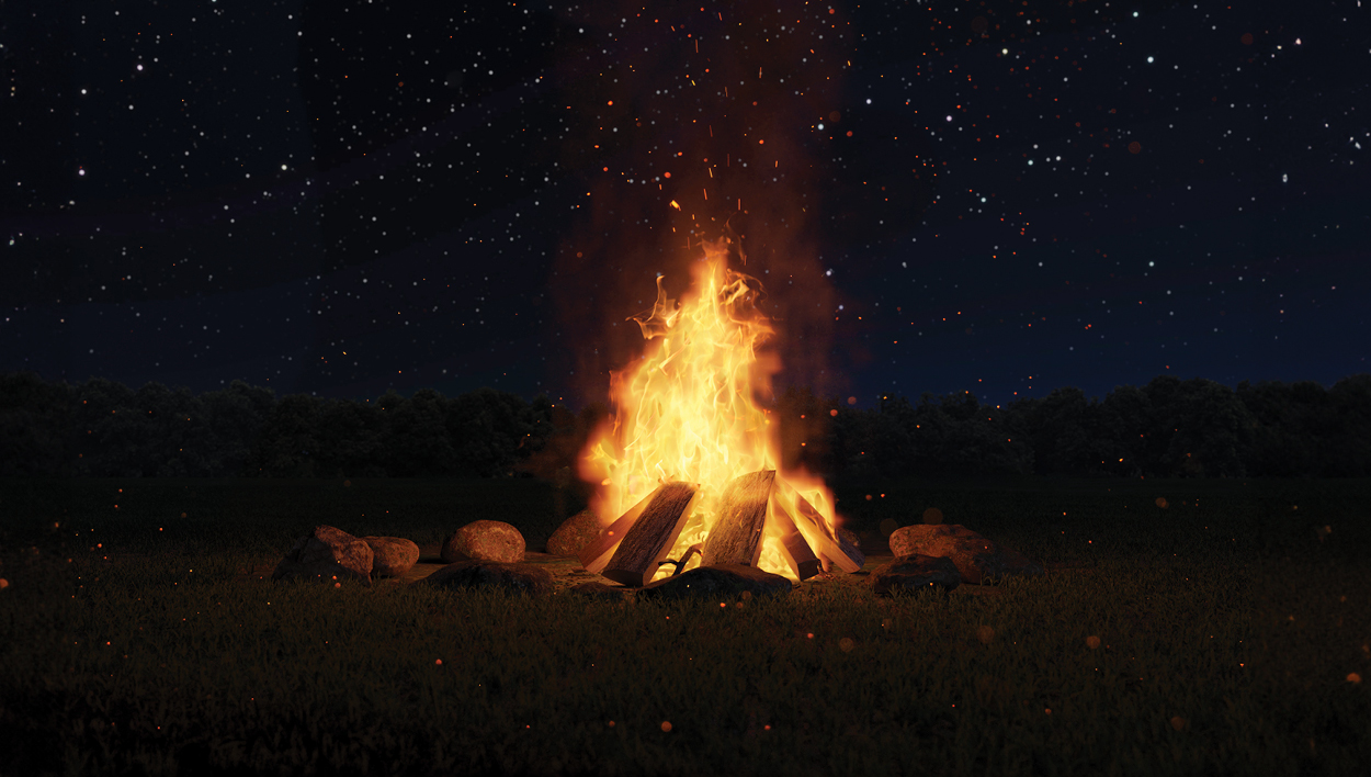 A bonfire is list in the night with the night sky in the background full of stars.