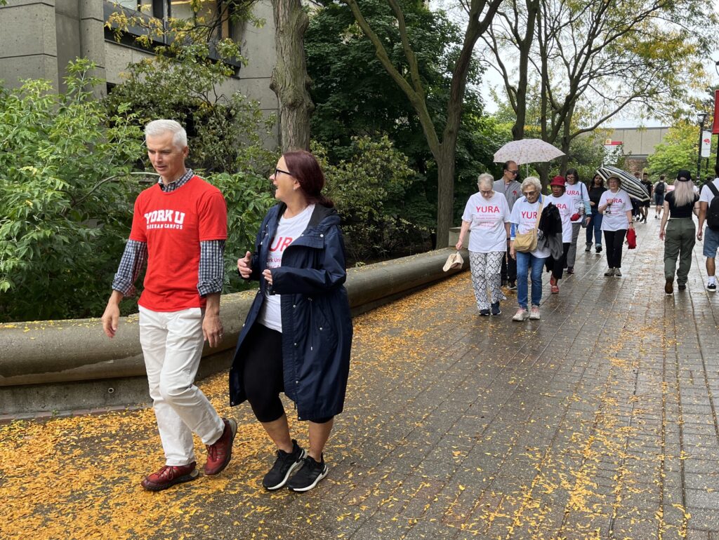 Art McDonald and Debbie Hansen walking along the Campus Walk near the Chemistry Building, with rest of the YURA participants some distance behind