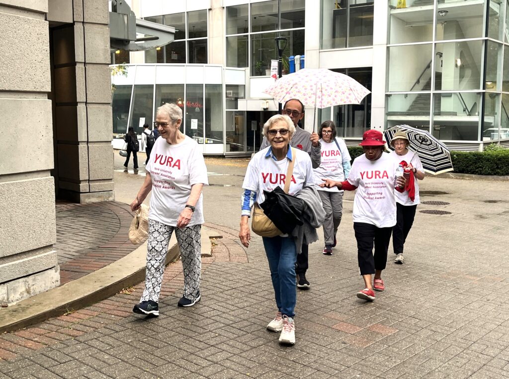 Lynn Taylor Claudia Hungerson and Agnes Fraser turning to corner from the Campus Walk onto the William McLean Walk adjacent to the Chemstry Building.  In the background, Steven Chuang and Diane Woody have opened their umbrellas.