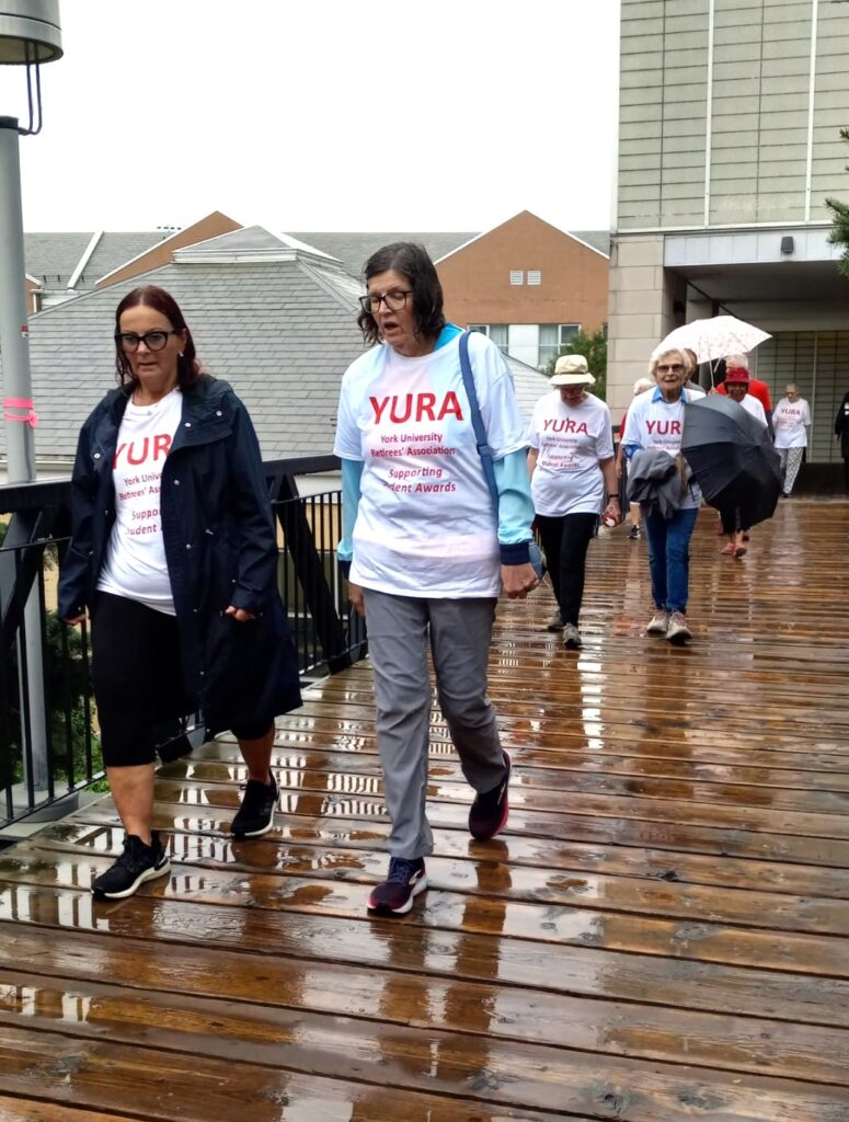 Debbie Hansen and Donna Smith walk across the pedestrian bridge from Calumet College to the Campus Walk, both looking quite soaked from the rain.  Diane Woody and Claudia Hungerson are in the background.